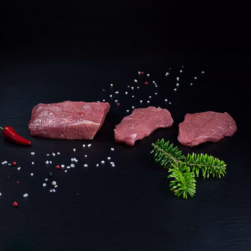 Rohe Wildschweinschnitzel mit Kräutern und Gewürzen auf dunklem Untergrund