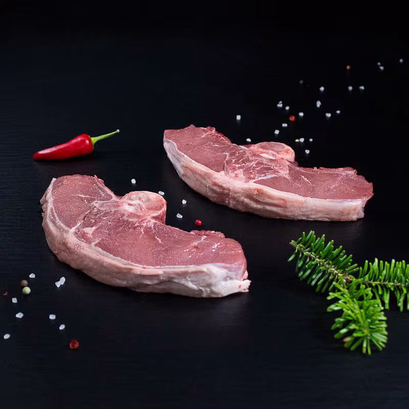Rohes Wildschweinkotelett mit Kräutern und Gewürzen auf dunklem Untergrund