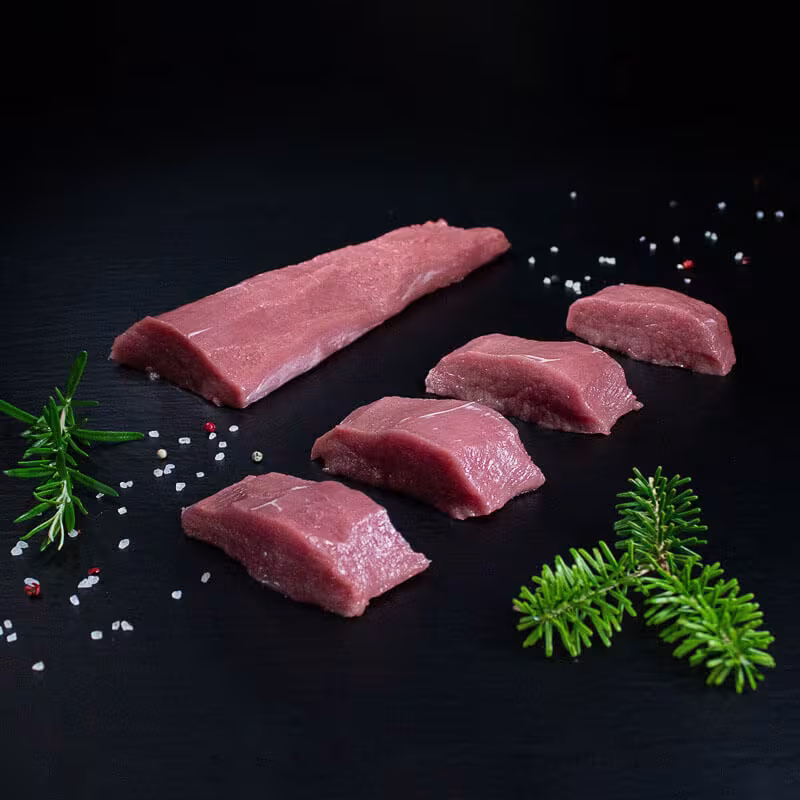 Rohe Wildschweinmedaillons mit Kräutern und Gewürzen auf dunklem Untergrund