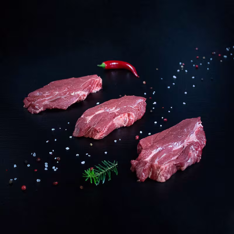 Rohe Wildschweinnackensteaks mit Kräutern und Gewürzen auf dunklem Untergrund