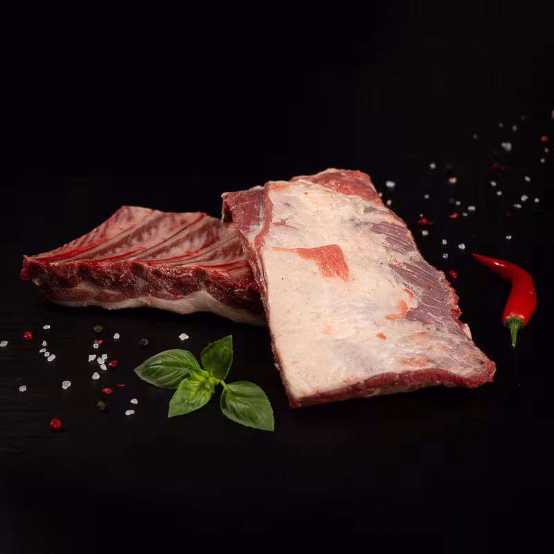 Rohe Grillrippchen vom Wildschwein mit Kräutern und Gewürzen auf dunklem Untergrund