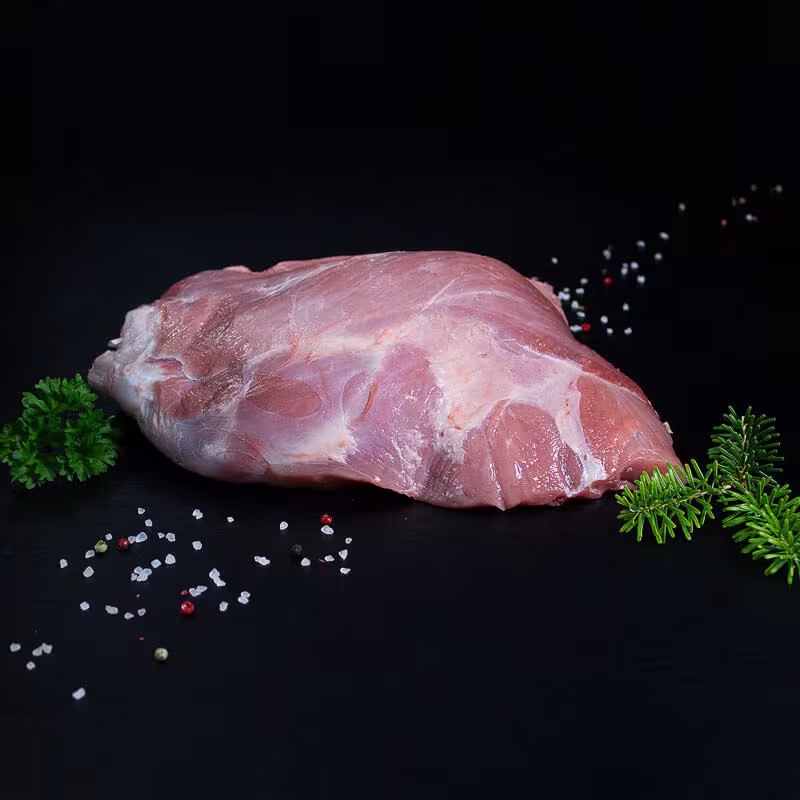Rohe Frischlingskeule mit Knochen, Pfeffer, Salz und Chili auf dunklem Untergrund