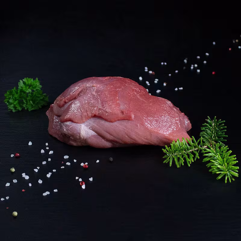 Roher Frischlingsbraten aus der Keule mit Kräutern und Gewürzen auf dunklem Untergrund