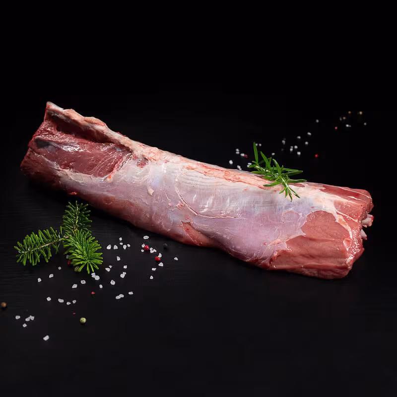 Roher Frischlingsrücken mit Knochen, Pfeffer, Salz und Chili auf dunklem Untergrund