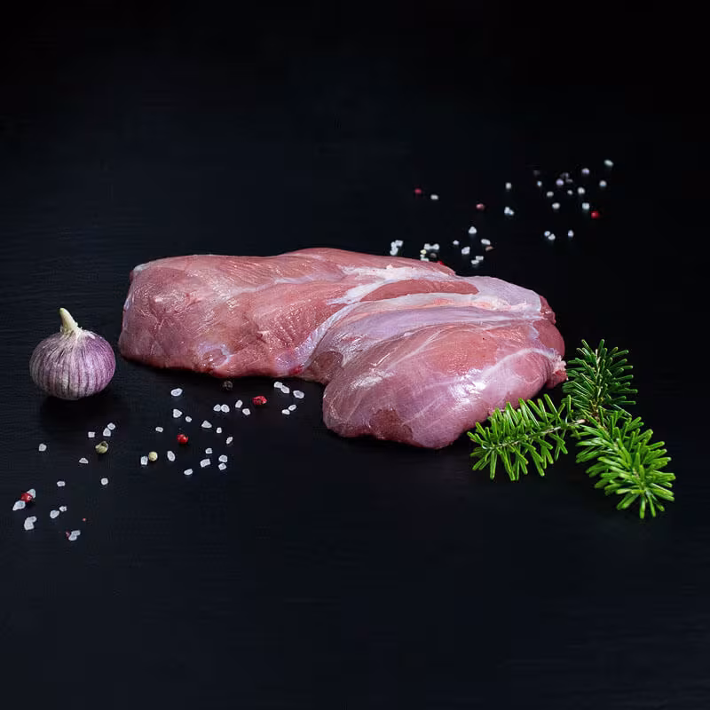 Rohe Frischlingsschulter mit Knochen, Pfeffer, Salz und Chili auf dunklem Untergrund
