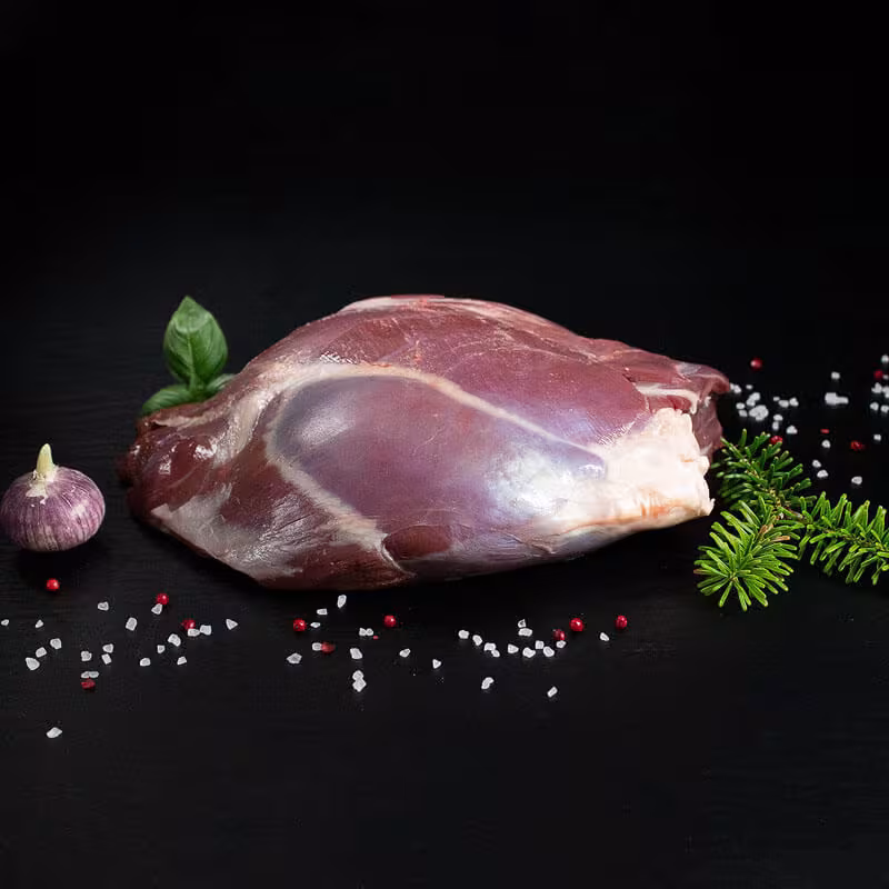 Rohe Rehkeule mit Knochen, Pfeffer, Salz und Chili auf dunklem Untergrund
