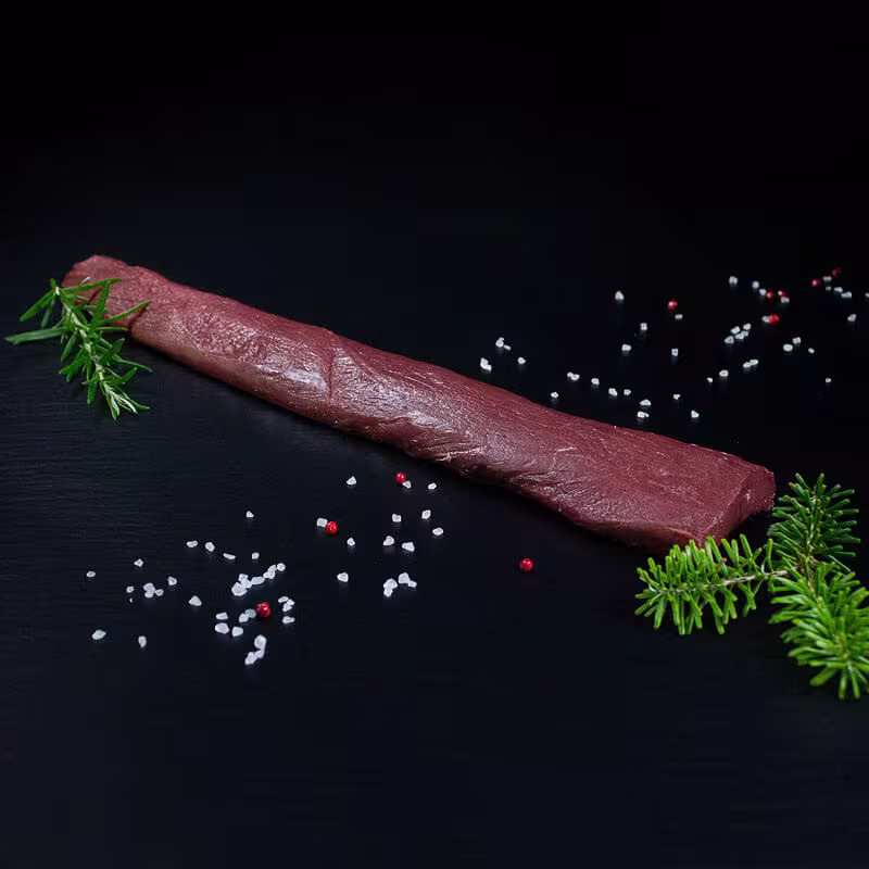 Roher parierter Rehrücken ohne Knochen mit Pfeffer, Salz und Chili auf dunklem Untergrund