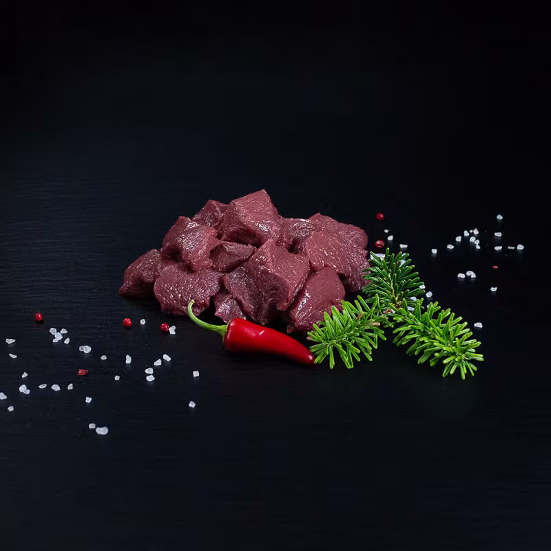 Rohes Rehgulasch mit Kräutern und Gewürzen auf dunklem Untergrund