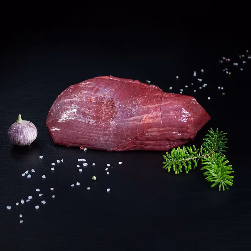 Roher Hirschbraten aus der Keule mit Kräutern und Gewürzen auf dunklem Untergrund
