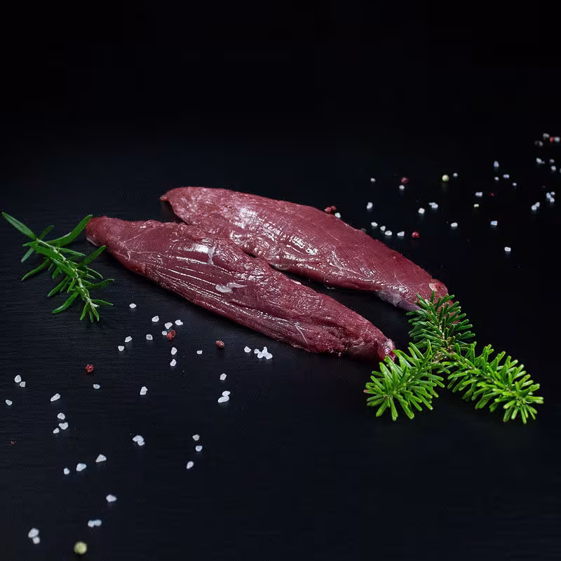 Rohes Hirschfilet mit Kräutern und Gewürzen auf dunklem Untergrund