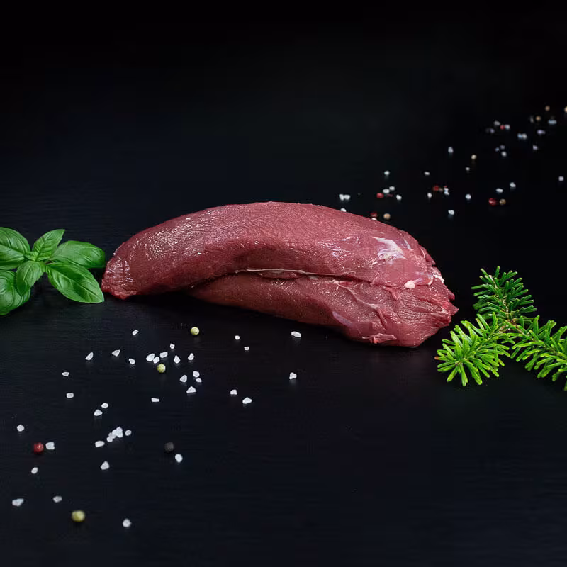 Roher Hirschbraten aus der Schulter mit Kräutern und Gewürzen auf dunklem Untergrund