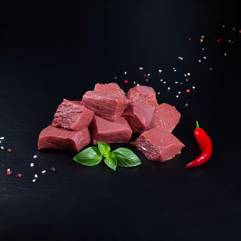 Rohes Hirschgulasch mit Kräutern und Gewürzen auf dunklem Untergrund