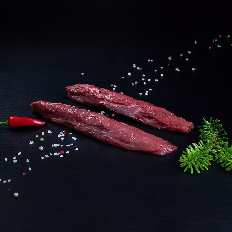 Rohe Wildschweinfilets mit Kräutern und Gewürzen auf dunklem Untergrund