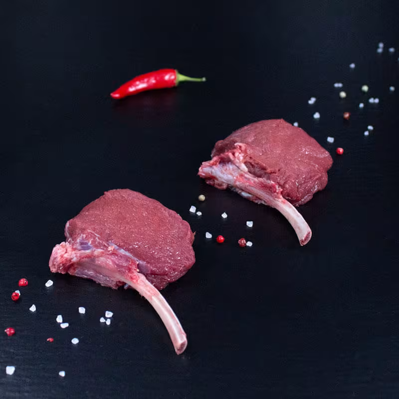 Rohe Hirsch-Tomahawk-Steaks mit Kräutern und Gewürzen auf dunklem Untergrund