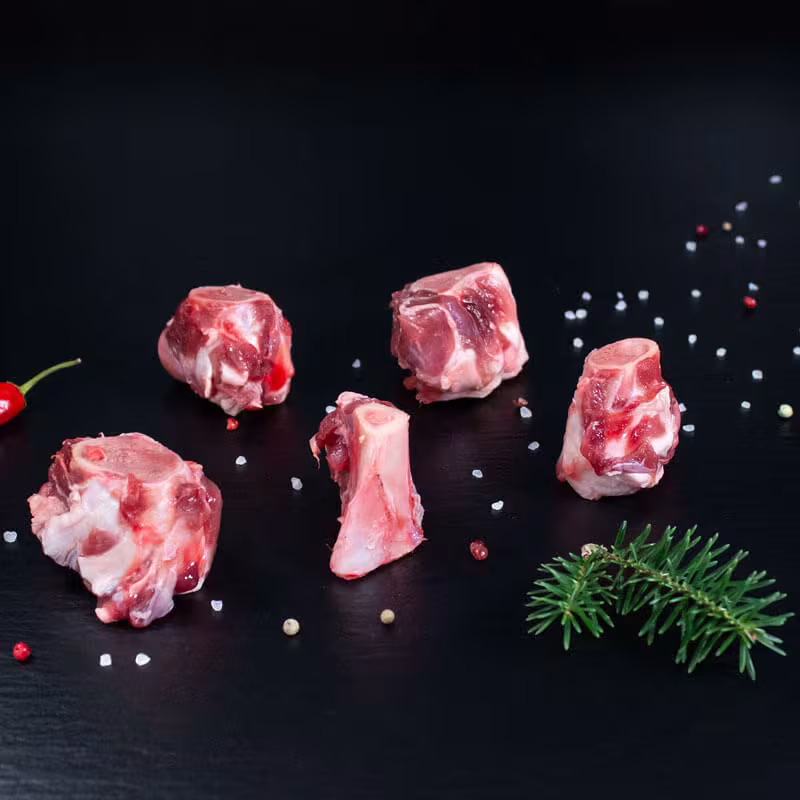 Rohe Wildschweinknochen für den Wildfond mit Pfeffer, Salz und Chili auf dunklem Untergrund