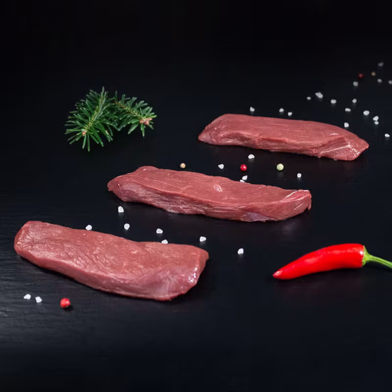 Rohe Rehsteaks mit Kräutern und Gewürzen auf dunklem Untergrund