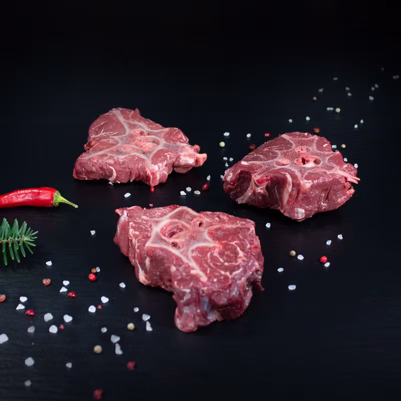 Drei rohe Hirschknochen mit Chili und Tannenzweig auf schwarzem Untergrund