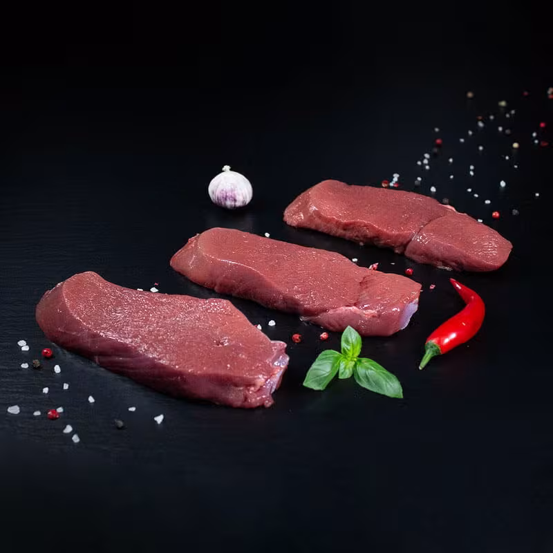 Rohe Hirschsteaks mit Kräutern und Gewürzen auf dunklem Untergrund