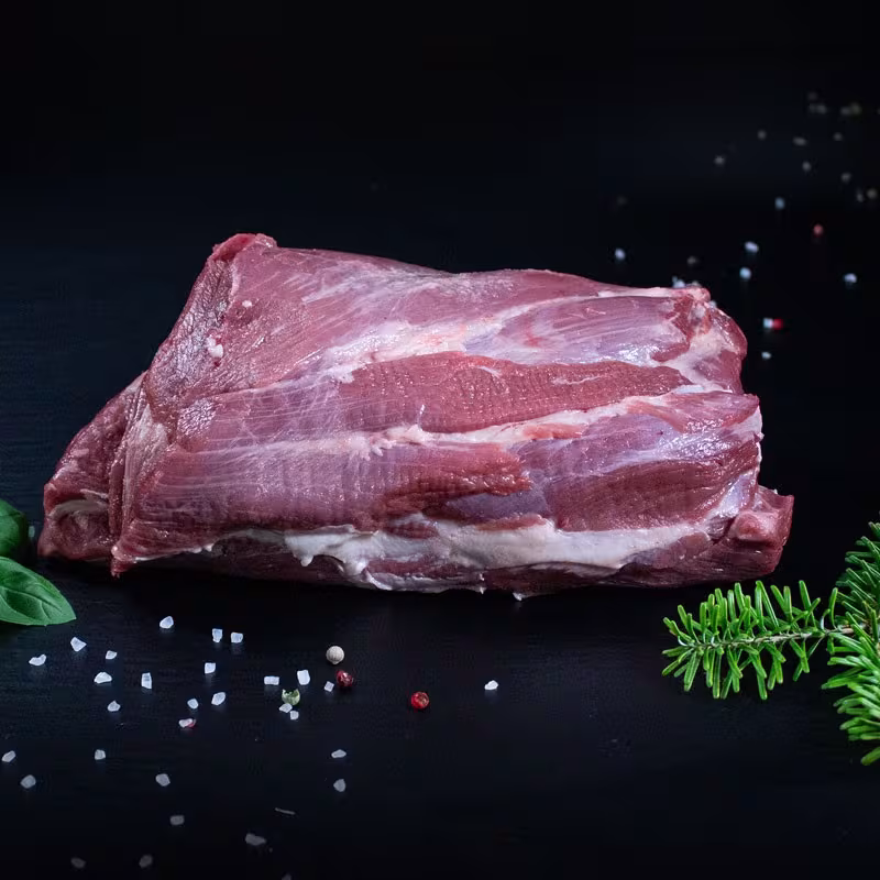 Roher Wildschweinnacken ohne Knochen mit Pfeffer, Salz und Chili auf dunklem Untergrund