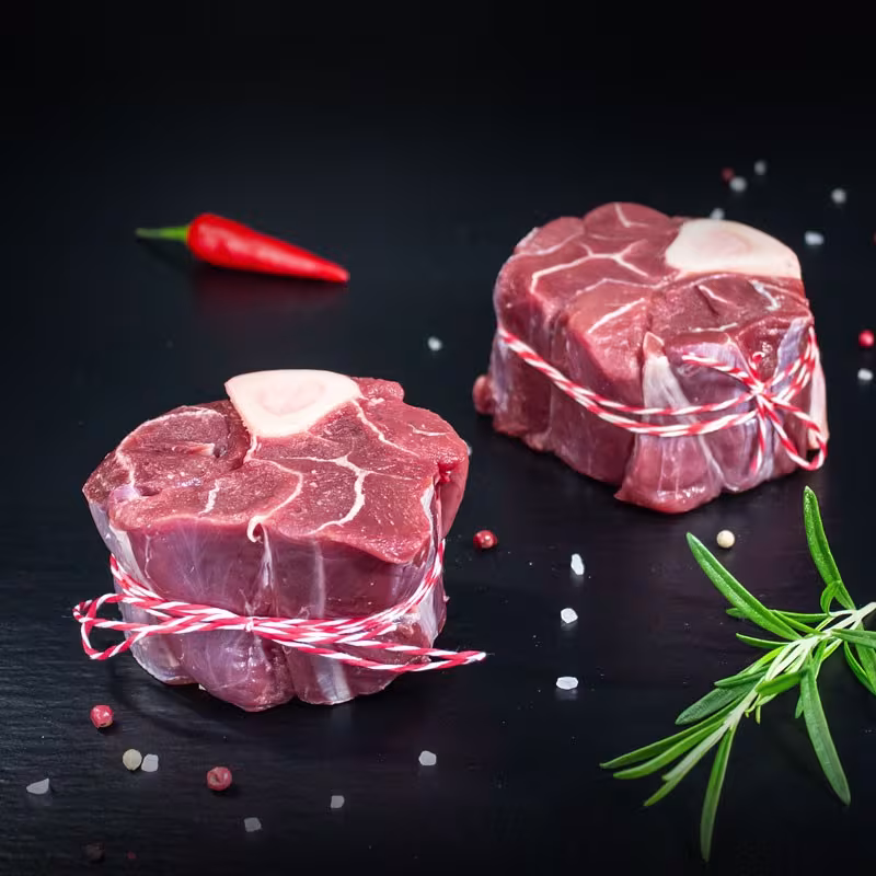 Rohe Hirsch-Ossobuco-Scheiben mit Kräutern und Gewürzen auf dunklem Untergrund