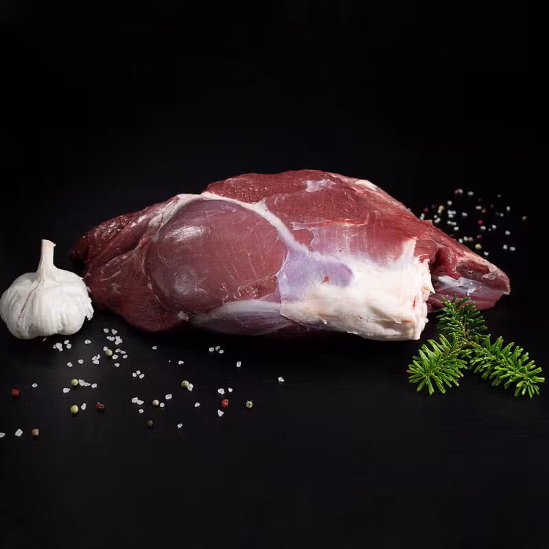 Rohe Hirschkalbskeule mit Knochen, Pfeffer, Salz und Chili auf dunklem Untergrund
