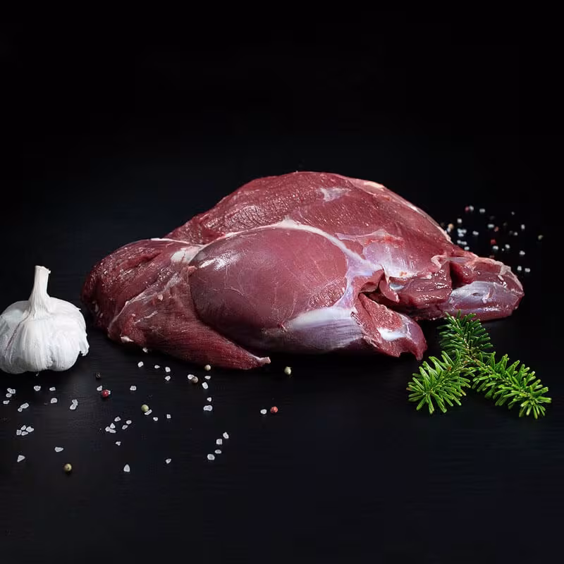 Rohe Hirschkalbskeule ohne Knochen mit Pfeffer, Salz und Chili auf dunklem Untergrund