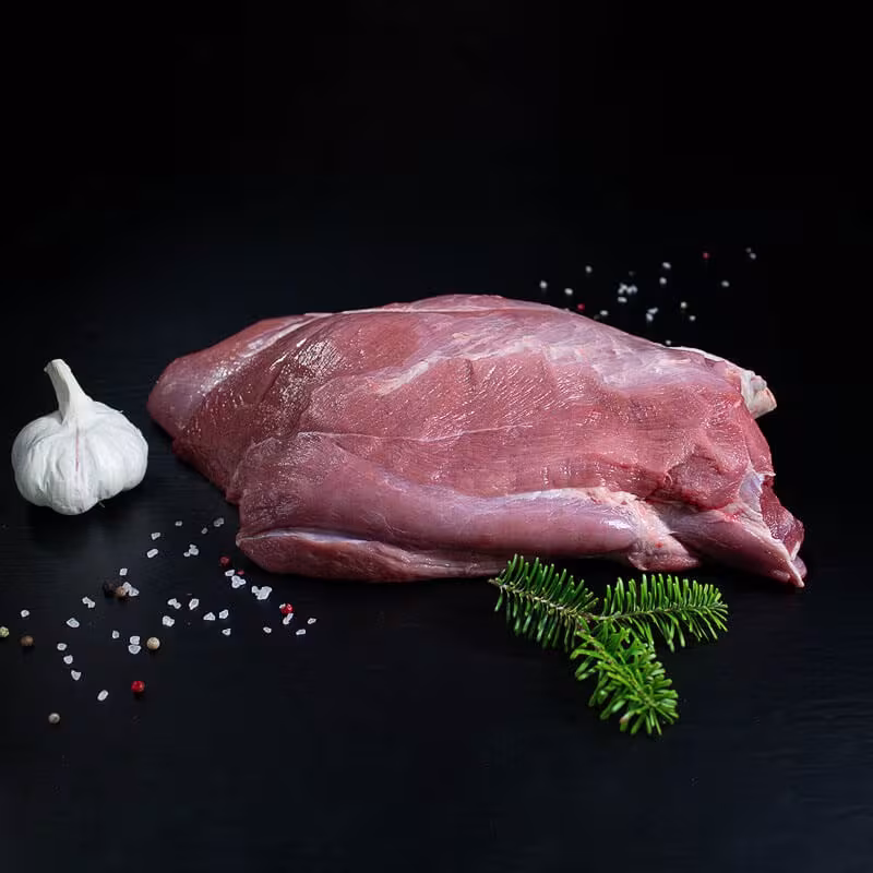 Rohe Wildschweinkeule ohne Knochen mit Pfeffer, Salz und Chili auf dunklem Untergrund