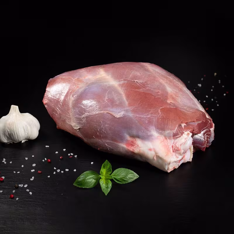 Rohe Wildschweinkeule mit Knochen, Pfeffer, Salz und Chili auf dunklem Untergrund