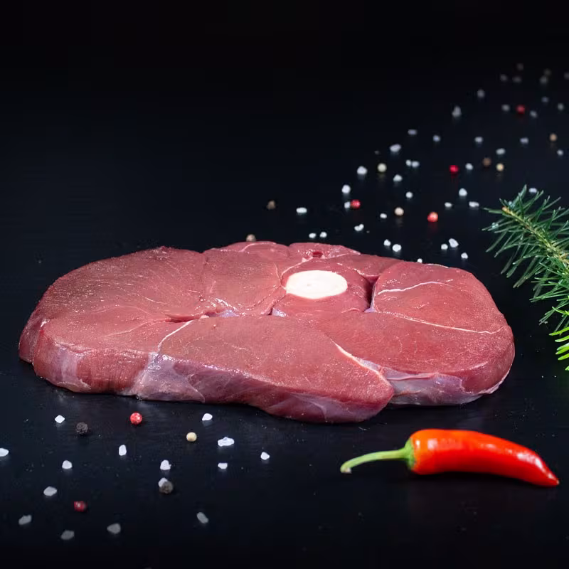 Rohe Hirsch-Holzfällersteaks mit Kräutern und Gewürzen auf dunklem Untergrund