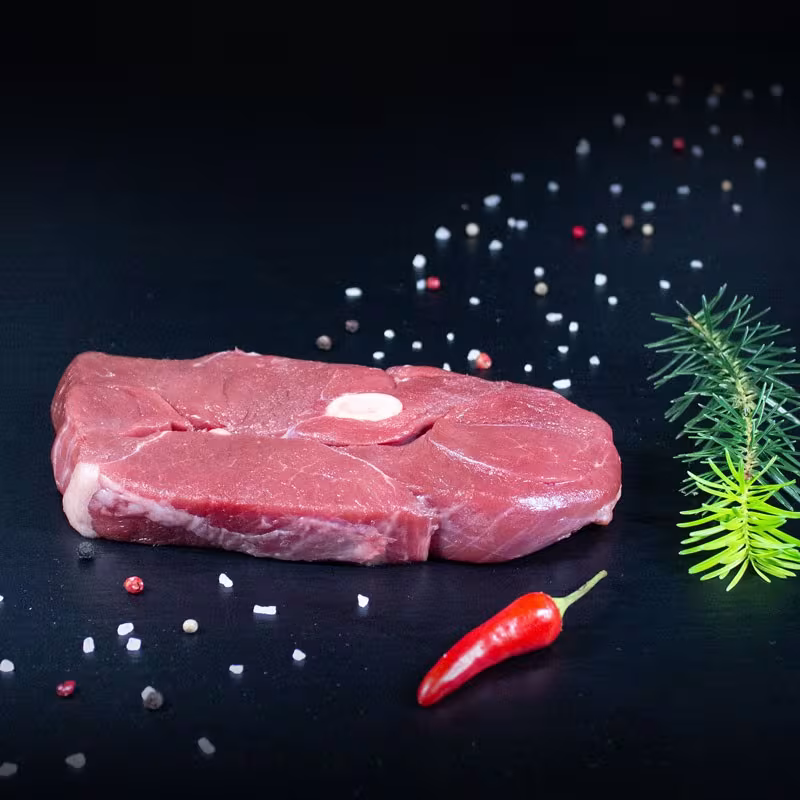 Rohe Wildschwein-Holzfällersteaks mit Kräutern und Gewürzen auf dunklem Untergrund