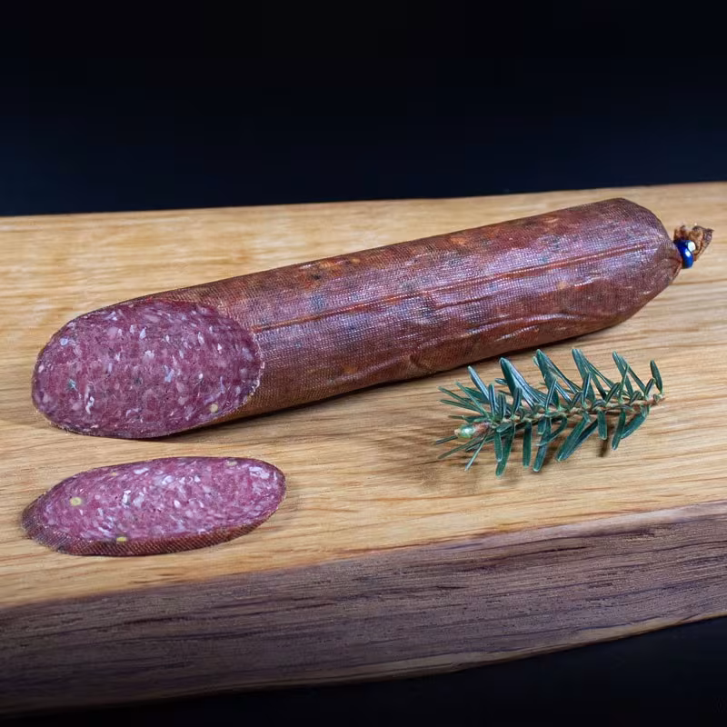 Wildsalami mit Kräutern und Gewürzen auf dunklem Untergrund
