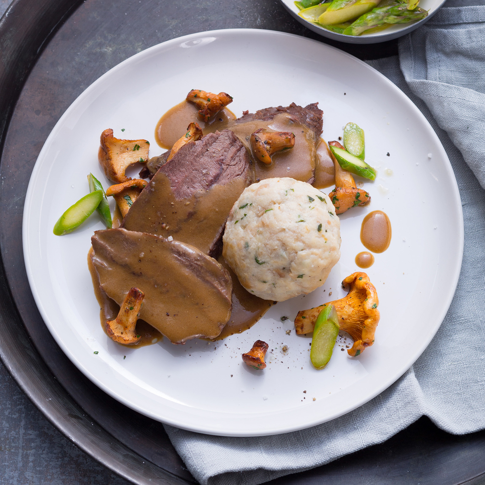 Aufgeschnittener Hirschbraten mit Pfifferlingen, Semmelknödel, grünem Spargel und dunkler Rahmsauce