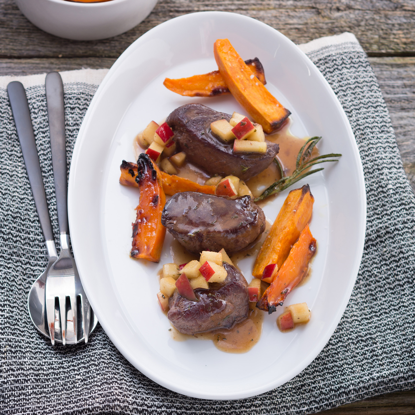 Hirschmedaillons mit Apfel-Honig-Sauce, roten Apfelwürfeln, gebratenen Möhren und Rosmarin