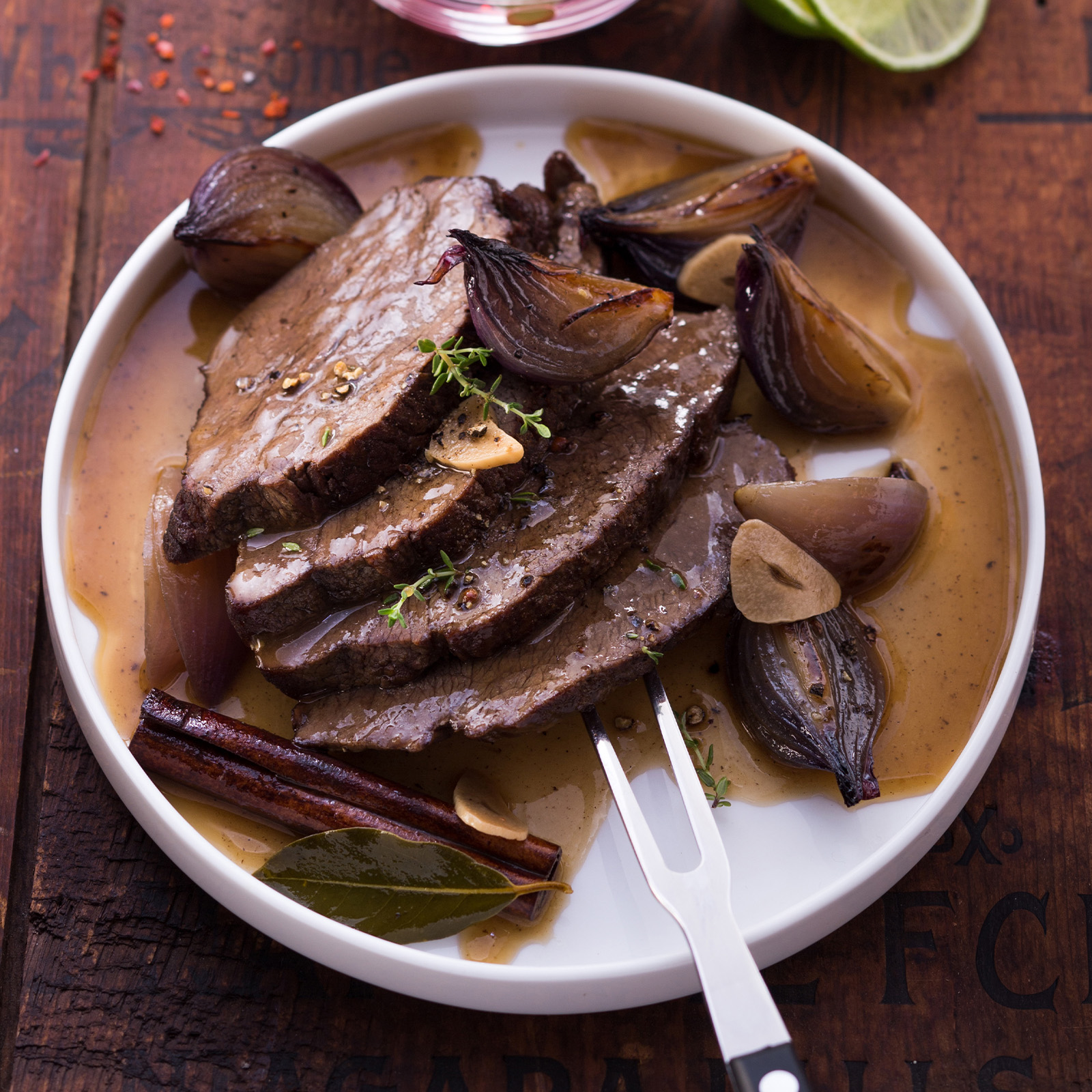 Aufgeschnittener Hirschbraten mit Rum, geschmorten roten Zwiebeln, Zimtstange, Lorbeer und Limette