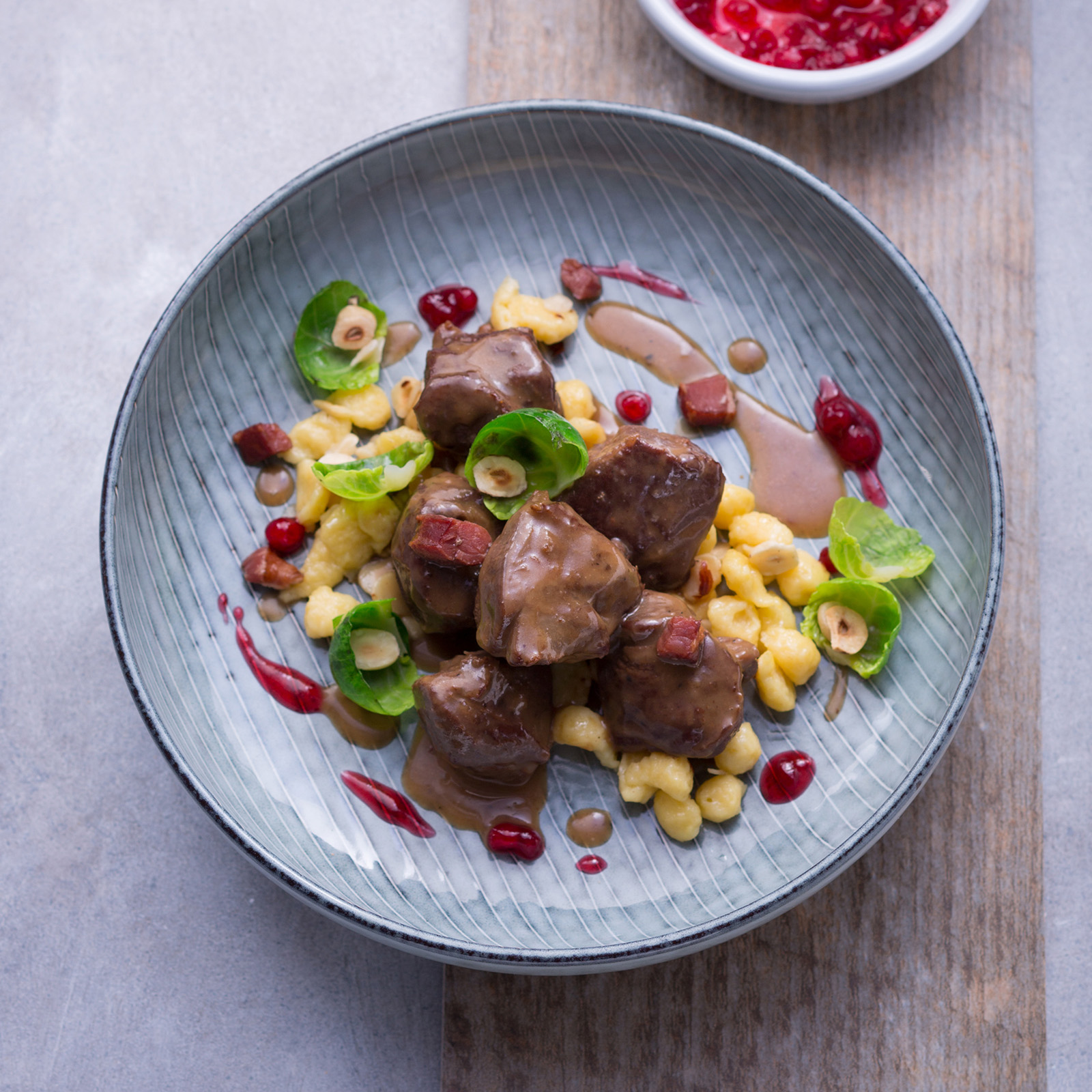 Rehgulasch mit Spätzle, Speckwürfeln, Preiselbeeren und Rosenkohlblättern in blauer Schale
