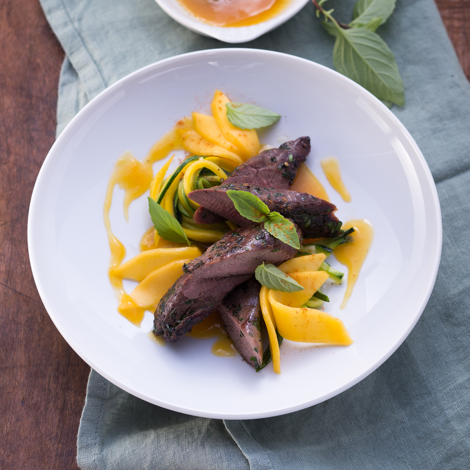 Kräuter-Rehfilets mit Mangosauce, Mangospalten, Zucchinistreifen und frischem Basilikum