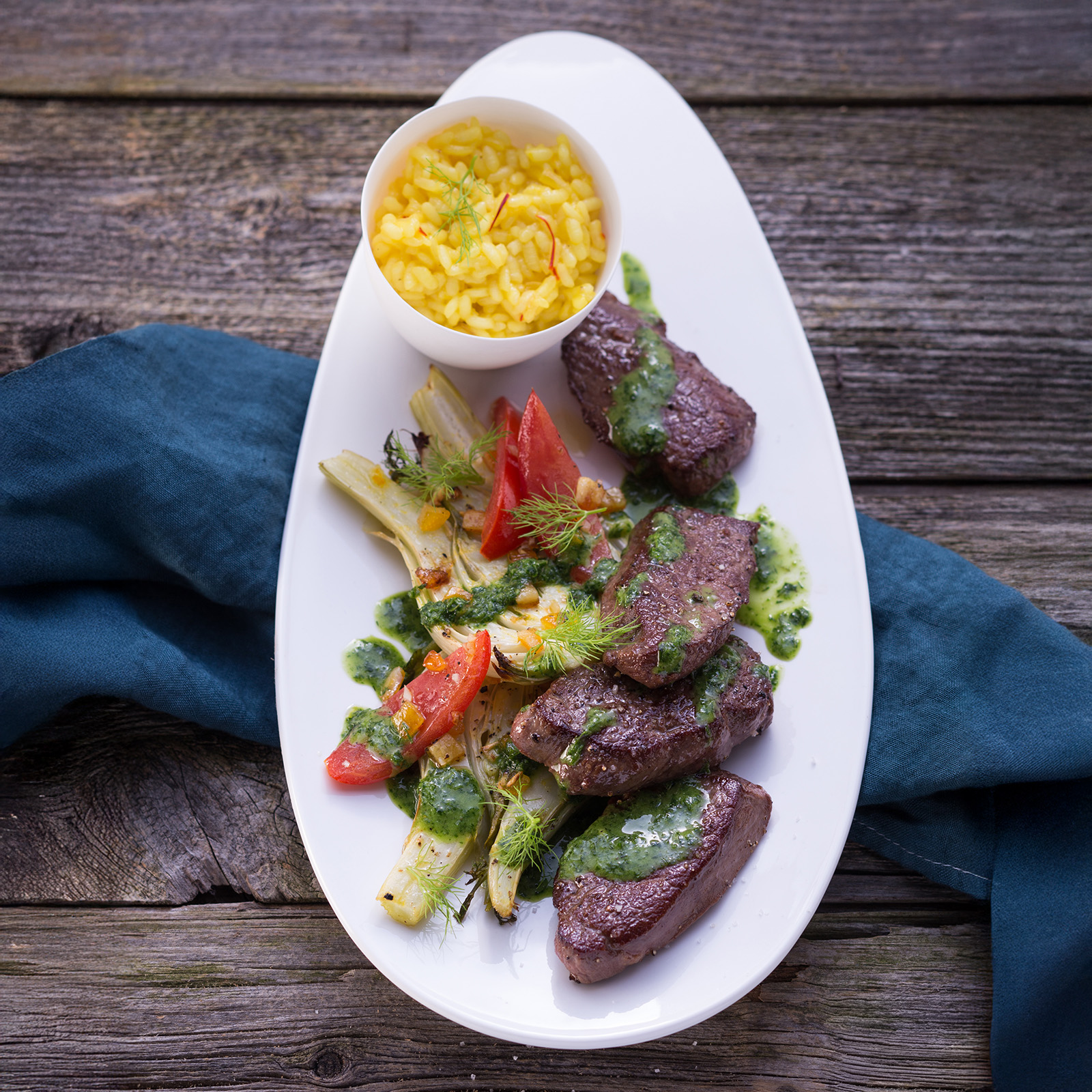 Gebratene Rehmedaillons mit Rucolasauce, Tomaten und Blattsalat auf ovalem Teller