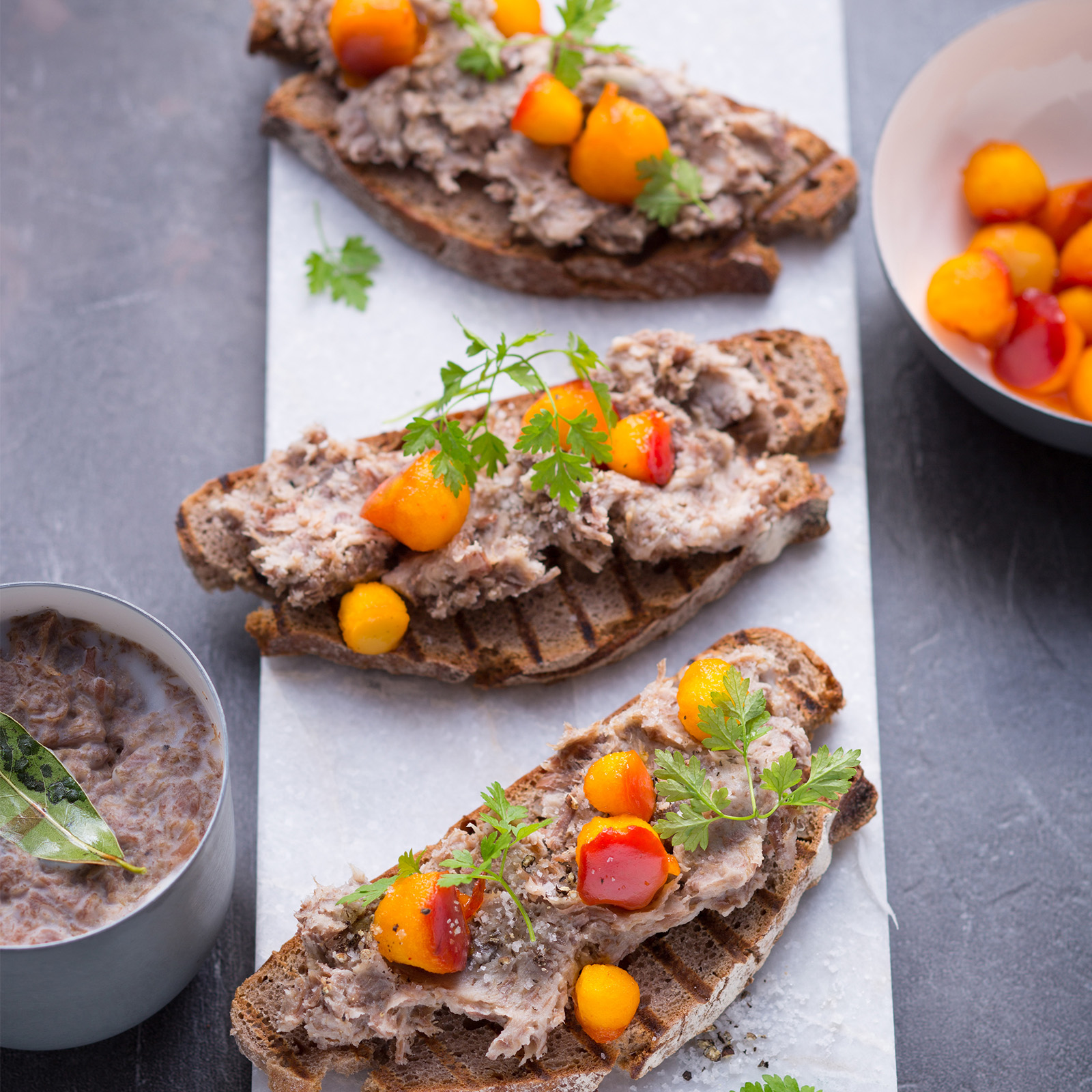 Wildschwein-Rillettes als grober Fleischaufstrich auf geröstetem Brot, garniert mit Kirschtomaten und frischen Kräutern