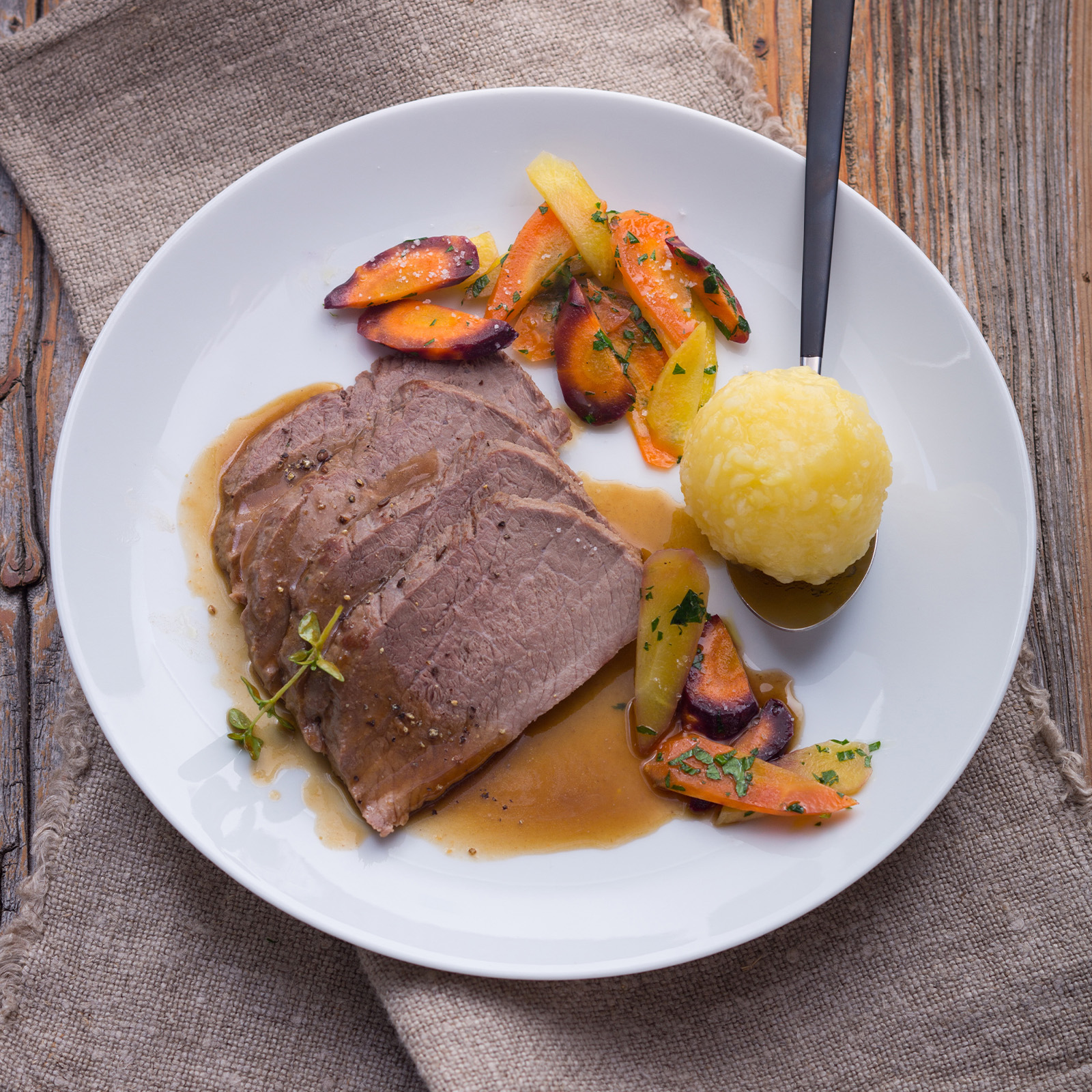 Aufgeschnittener Wildschweinbraten mit Semmelkloß, glasierten Karotten und dunkler Bratensauce