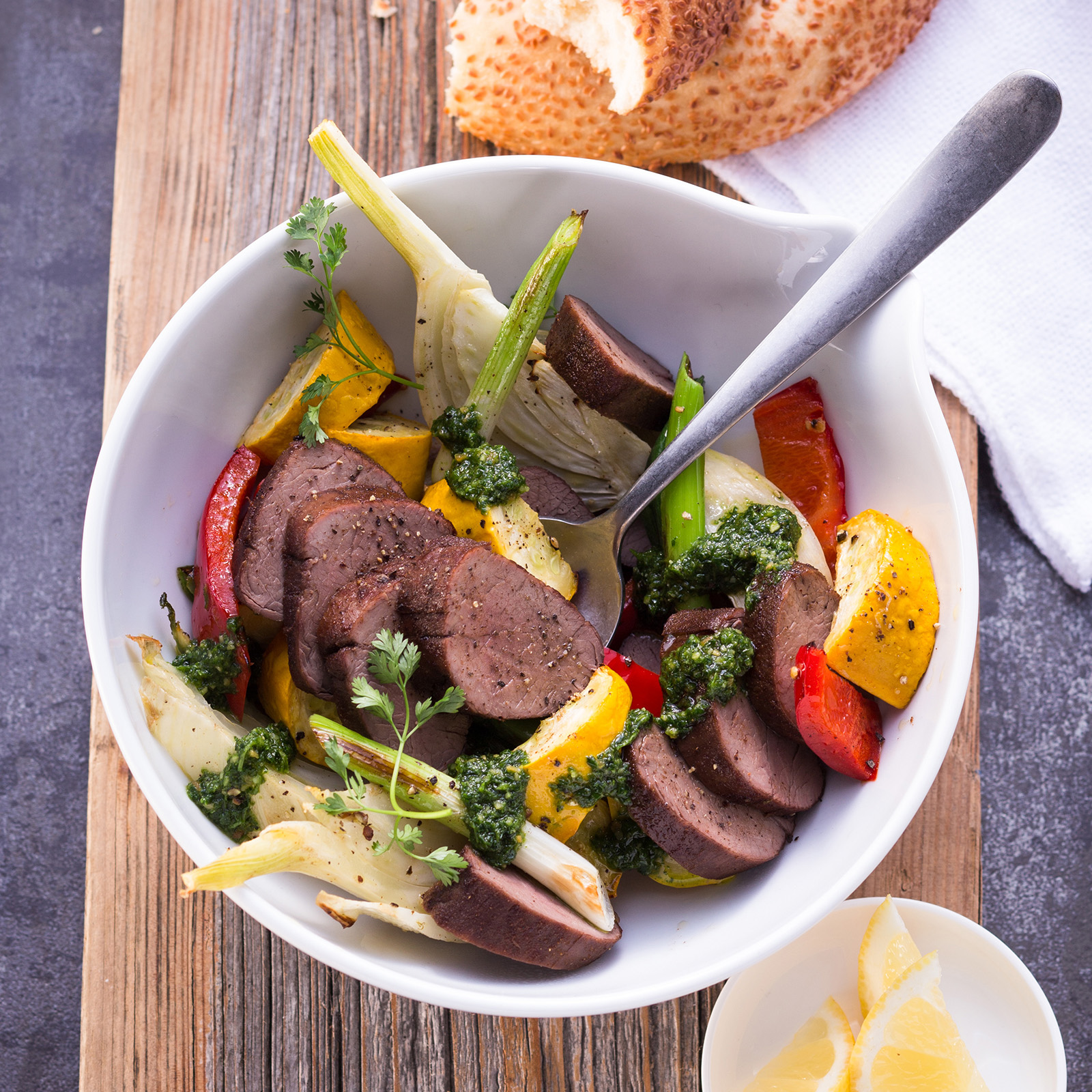 Aufgeschnittenes Wildschweinfilet mit Ofengemüse aus Paprika, Zucchini und Fenchel in einer Schale
