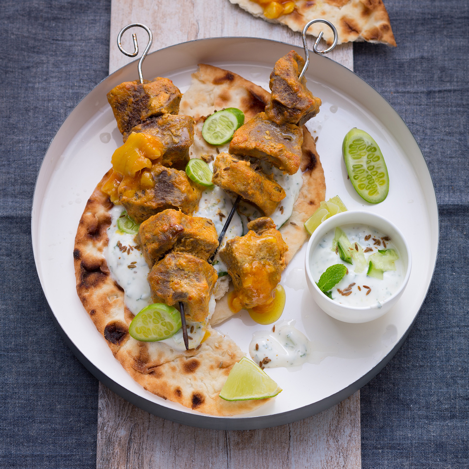 Tandoori-Wildschweinspieße mit Kürbis auf Fladenbrot, dazu Joghurtdip und Limettenspalten