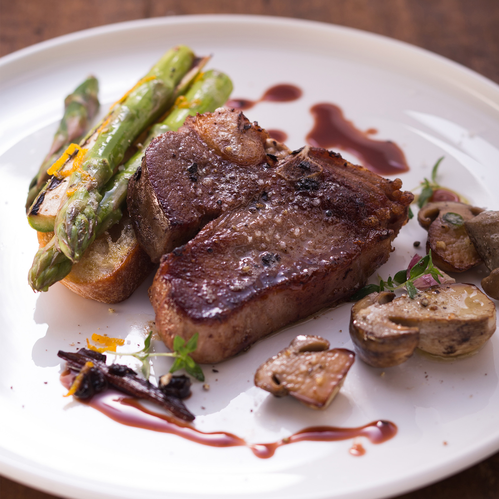 Gebratenes Wildschweinkotelett mit Steinpilzen, grünem Spargel und dunkler Grappa-Sauce