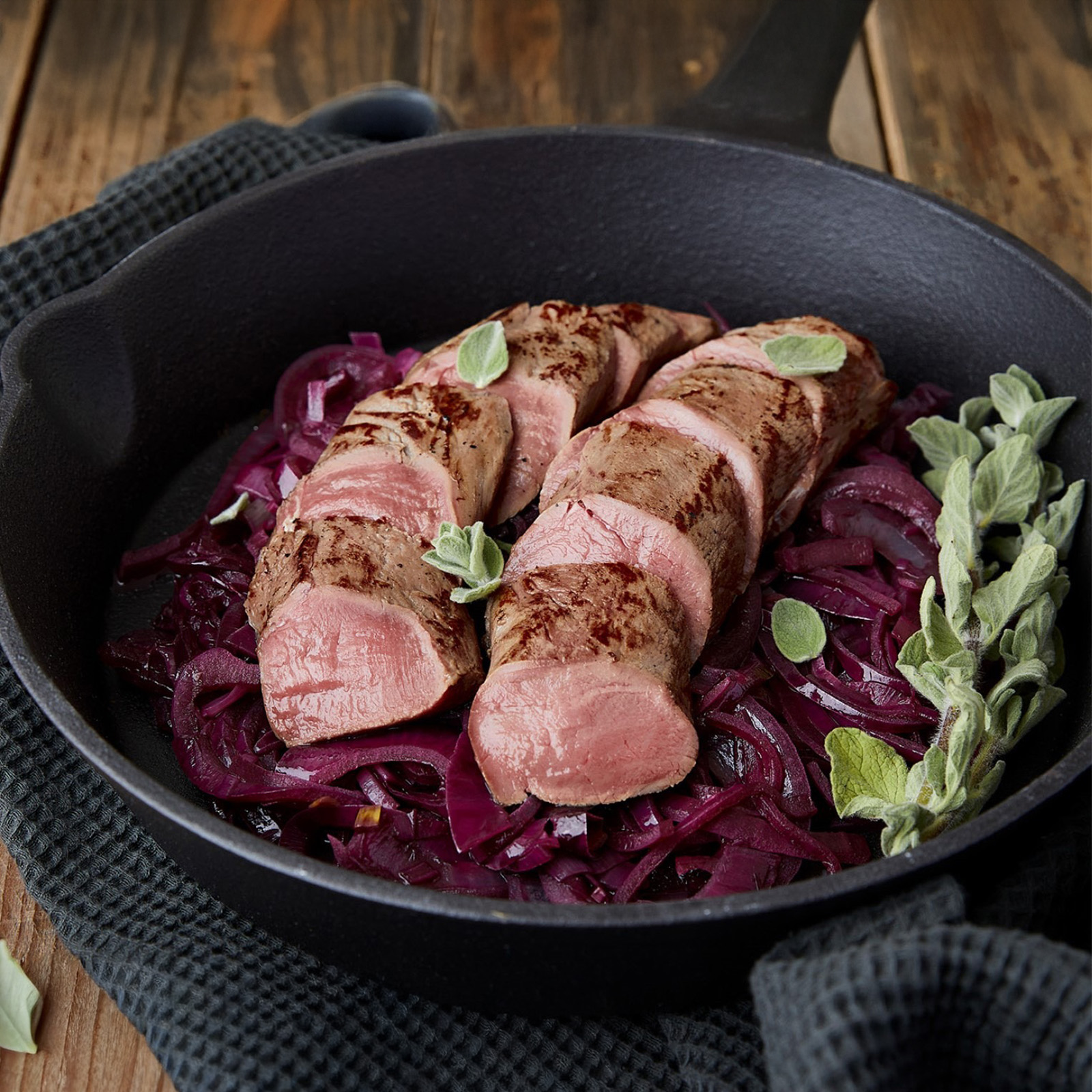 Rosa gebratener Rehrücken in der gusseisernen Pfanne auf Rotkohl mit Salbeiblättern