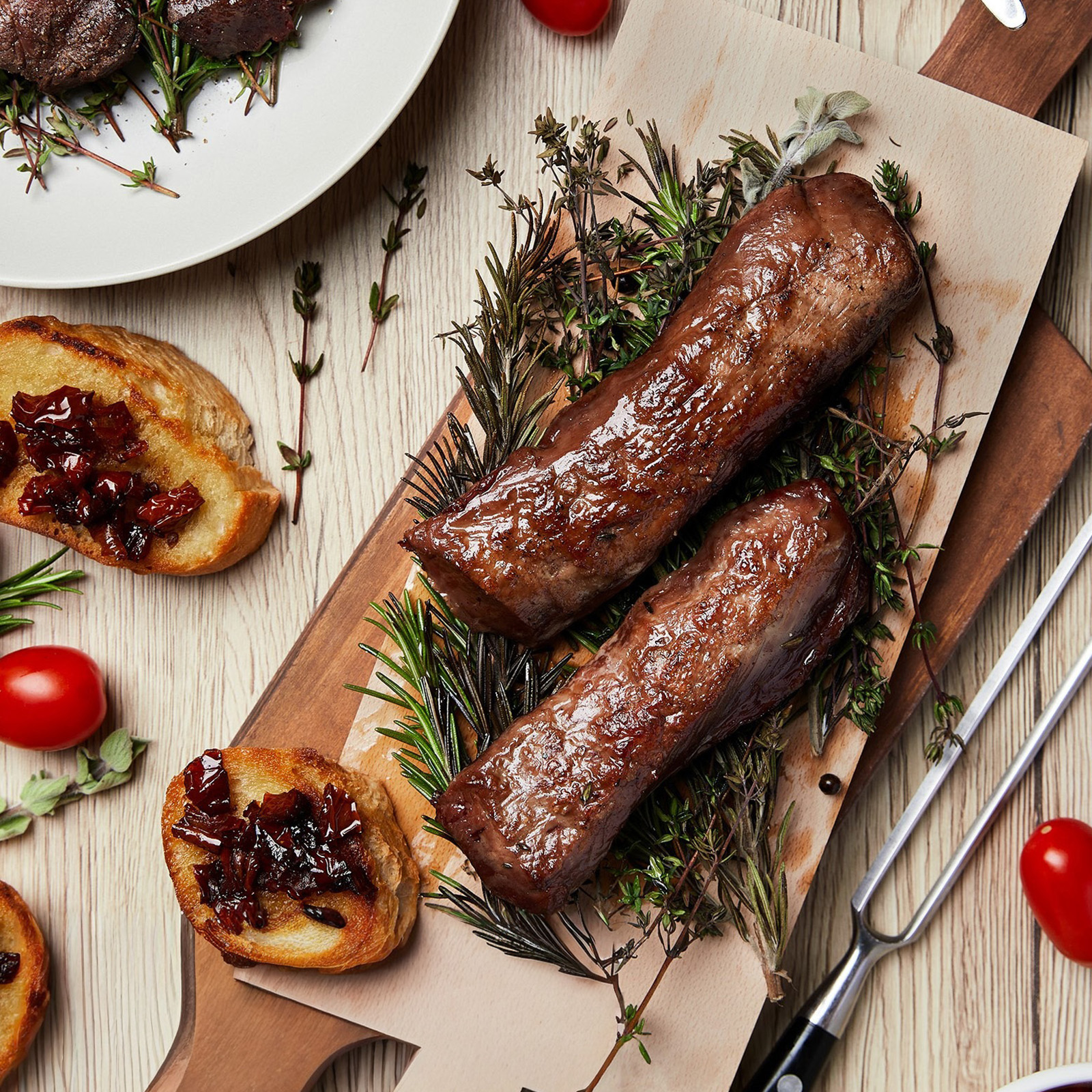 Gegrillte Wildfleischstücke auf einem Kräuterbett mit Crostini und Preiselbeeren auf Holzbrett
