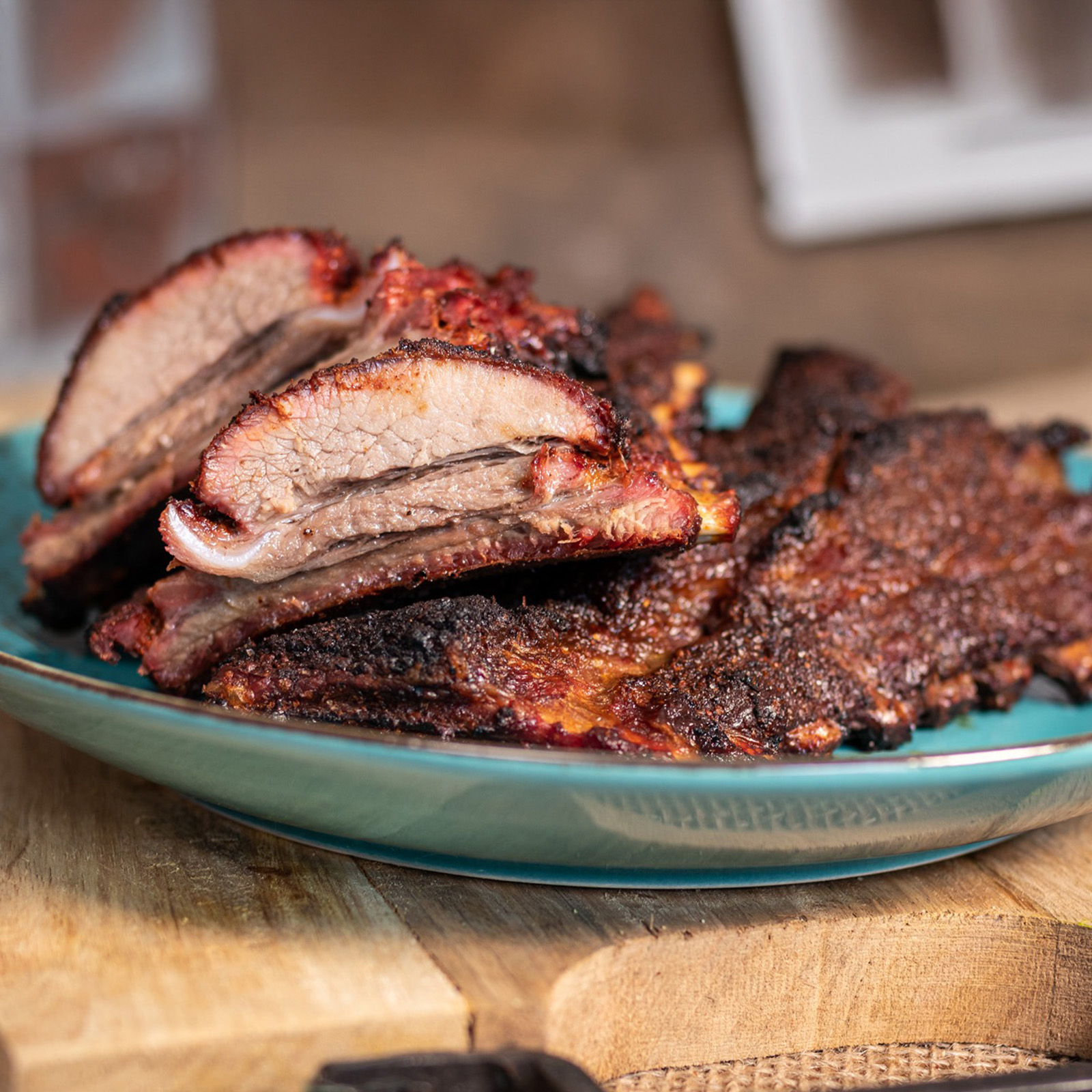 Glasierte Wildschwein-Spareribs nach der 3-2-1-Methode mit dunkler BBQ-Kruste auf türkisem Teller