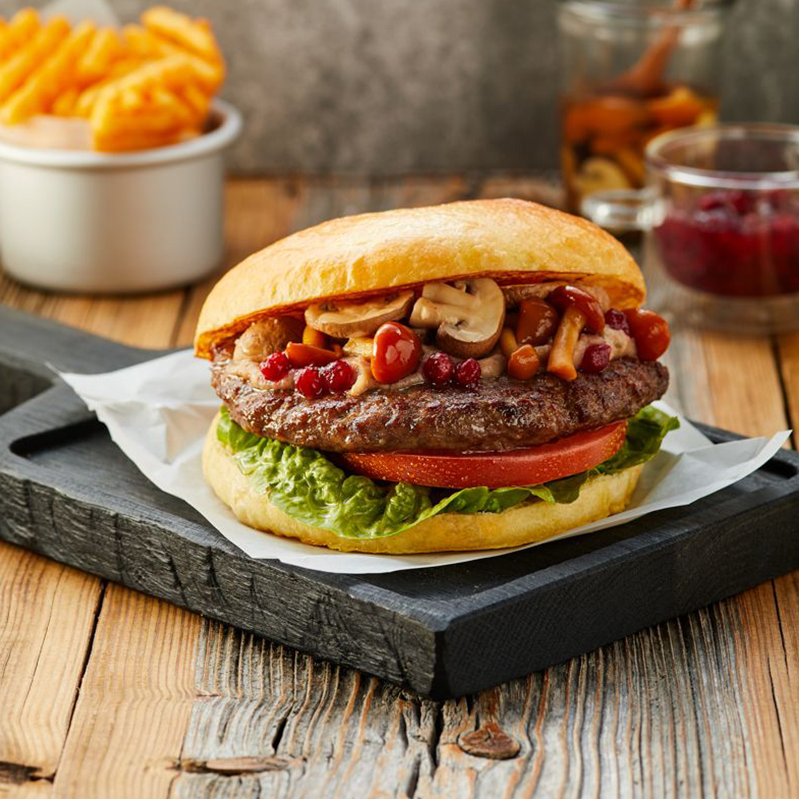 Wildschweinburger mit Waldpilzen, Preiselbeeren, Tomate und Salat im Brötchen, dazu Pommes frites