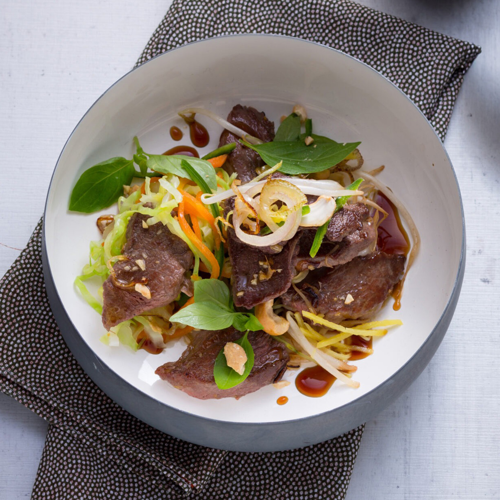 Wildschwein-Wok mit Cashewnüssen, Sojabohnensprossen, Gemüsestreifen und Thai-Basilikum in weißer Schale