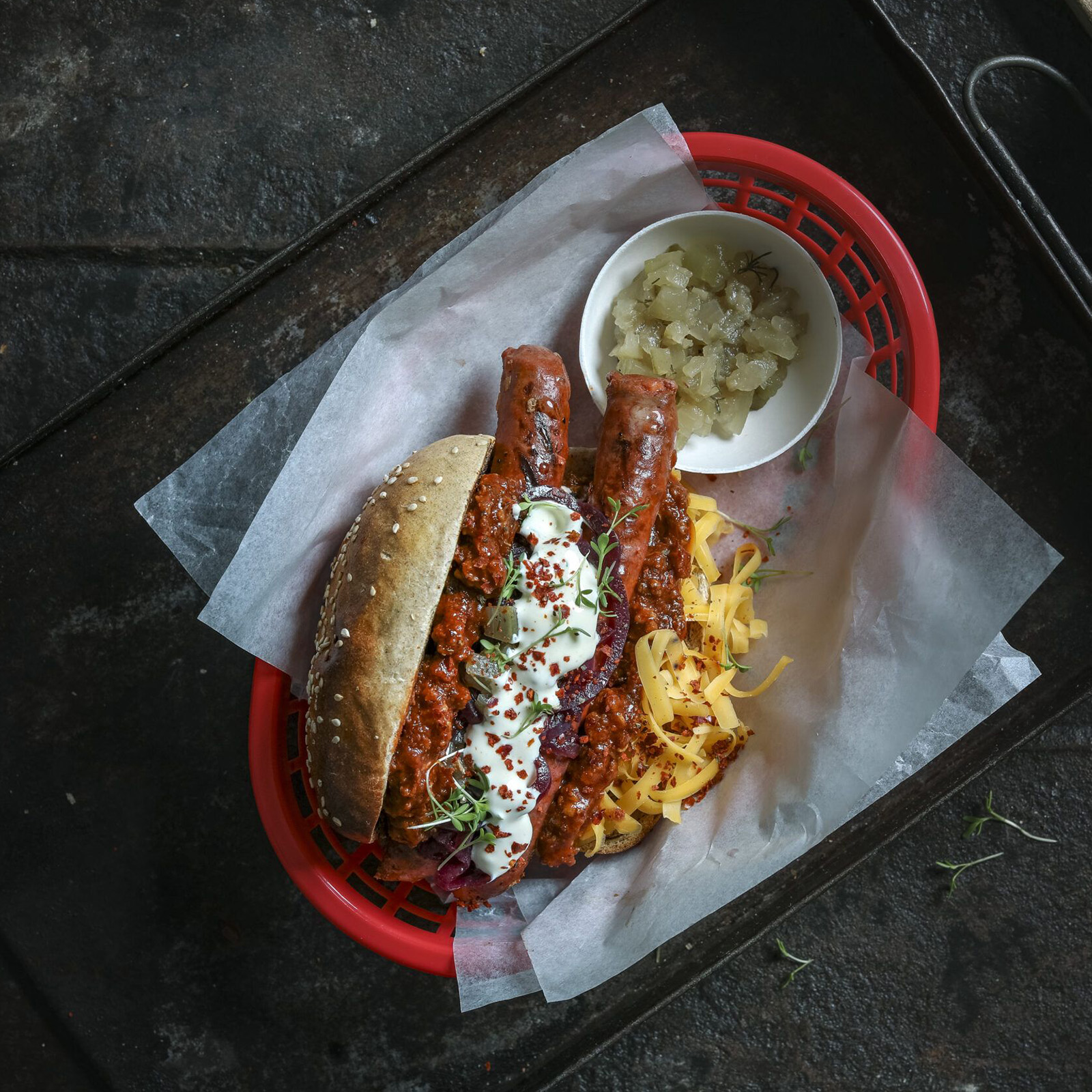 Hot Dog mit Wildbratwurst, Hackfleisch-Chili, Sauerrahm und geriebenem Käse im Körbchen