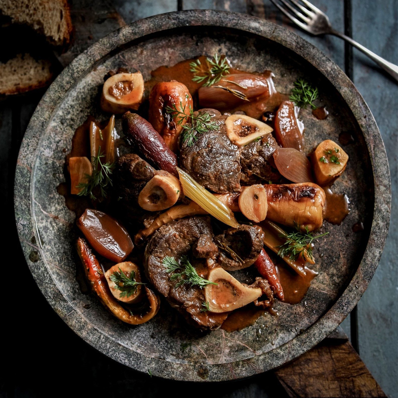 Geschmortes Hirsch-Ossobuco mit Markknochen, Wurzelgemüse und frischen Kräutern in rustikaler Pfanne