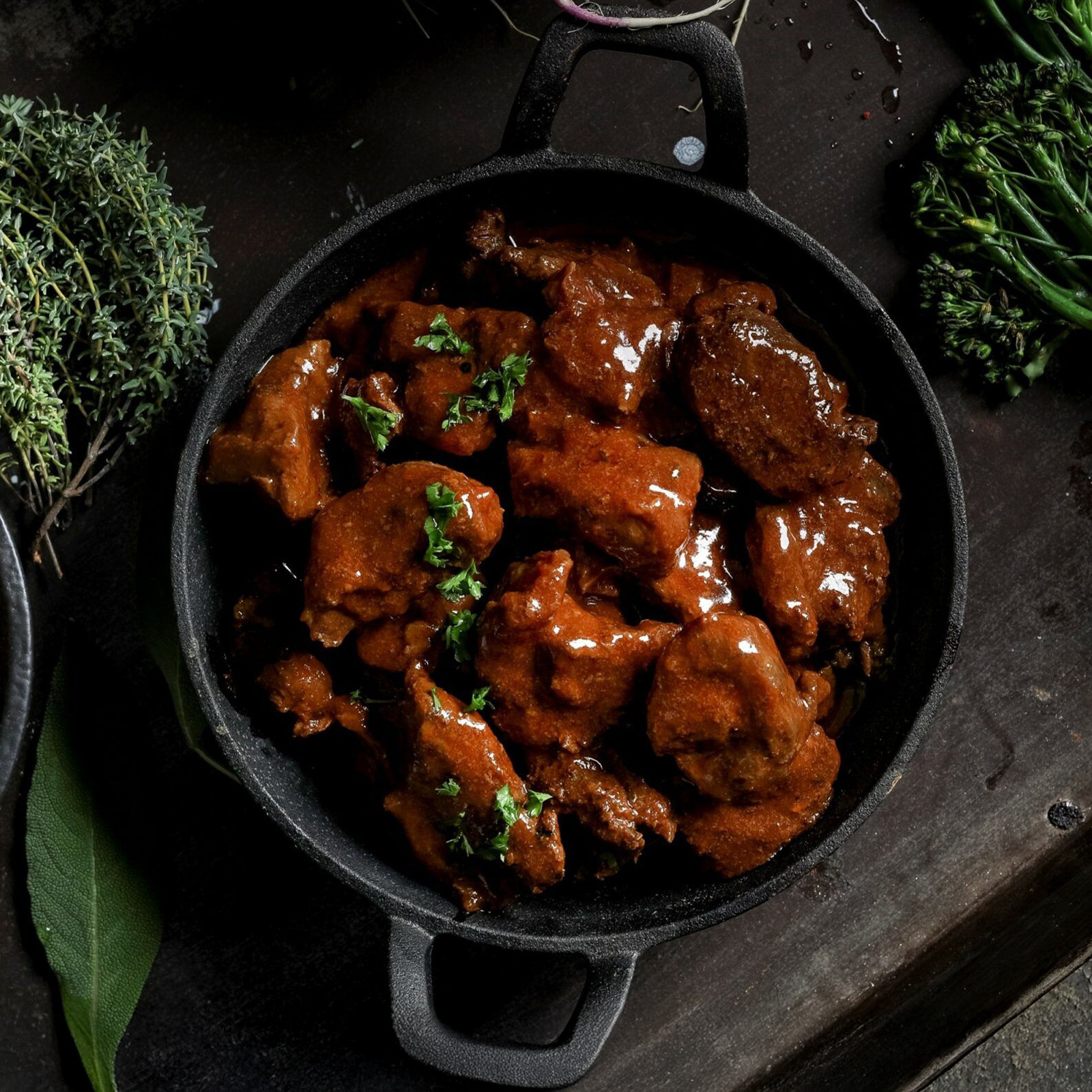 Hirschgulasch in dunkler Malzbier-Lebkuchen-Sauce im gusseisernen Topf mit frischen Kräutern